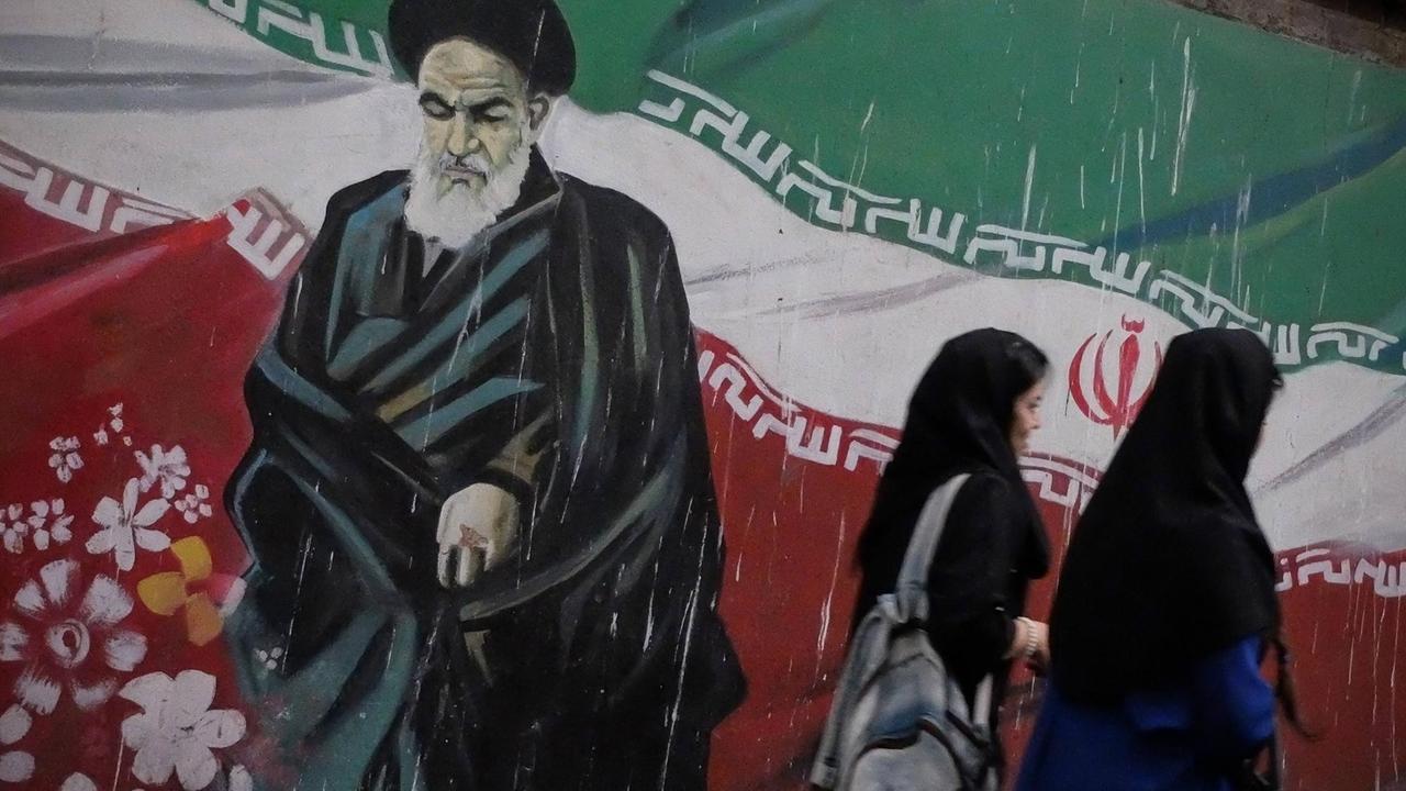 Zwei iranische Frauen vor einem Wandgemälde, das den Gründer der Islamischen Republik Iran, Ayatollah Ruhollah Khomeini, zeigt Zwei iranische Frauen vor einem Wandgemälde, das den Gründer der Islamischen Republik Iran, Ayatollah Ruhollah Khomeini, zeigt