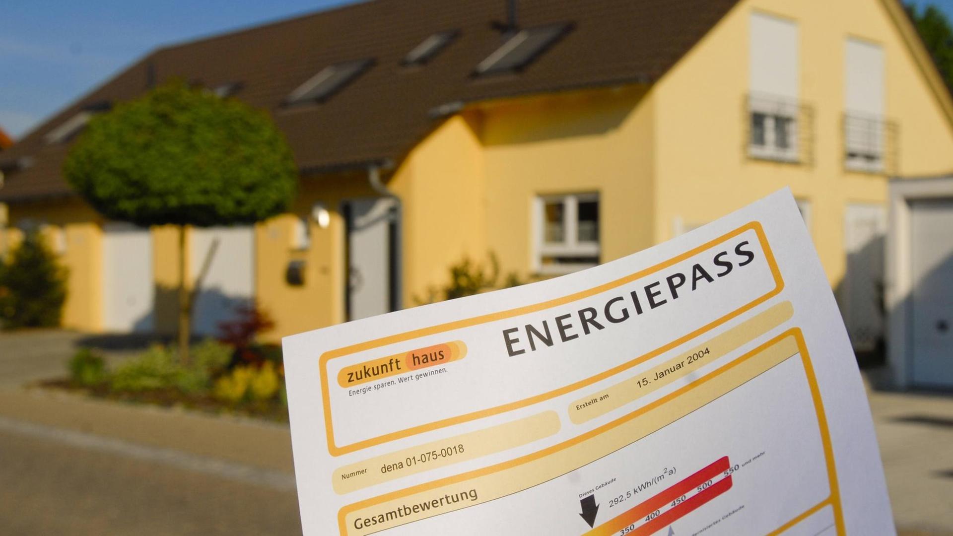Ein Energiepass für Immobilien ist im Vordergrund zu sehen. Im Hintergrund ein gelb angestrichenes Haus mit Garage.