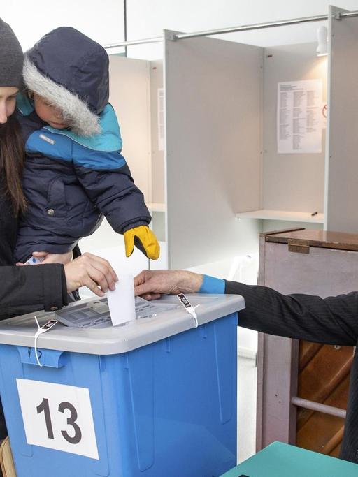 Eine Frau mit einem Kind auf dem Arm wirft in Tallinn ihren Wahlzettel in eine Urne.