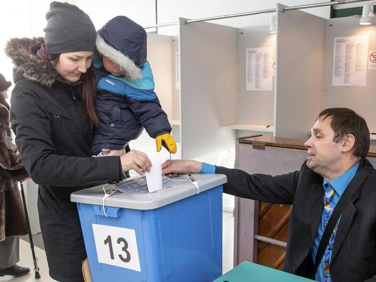 Eine Frau mit einem Kind auf dem Arm wirft in Tallinn ihren Wahlzettel in eine Urne.
