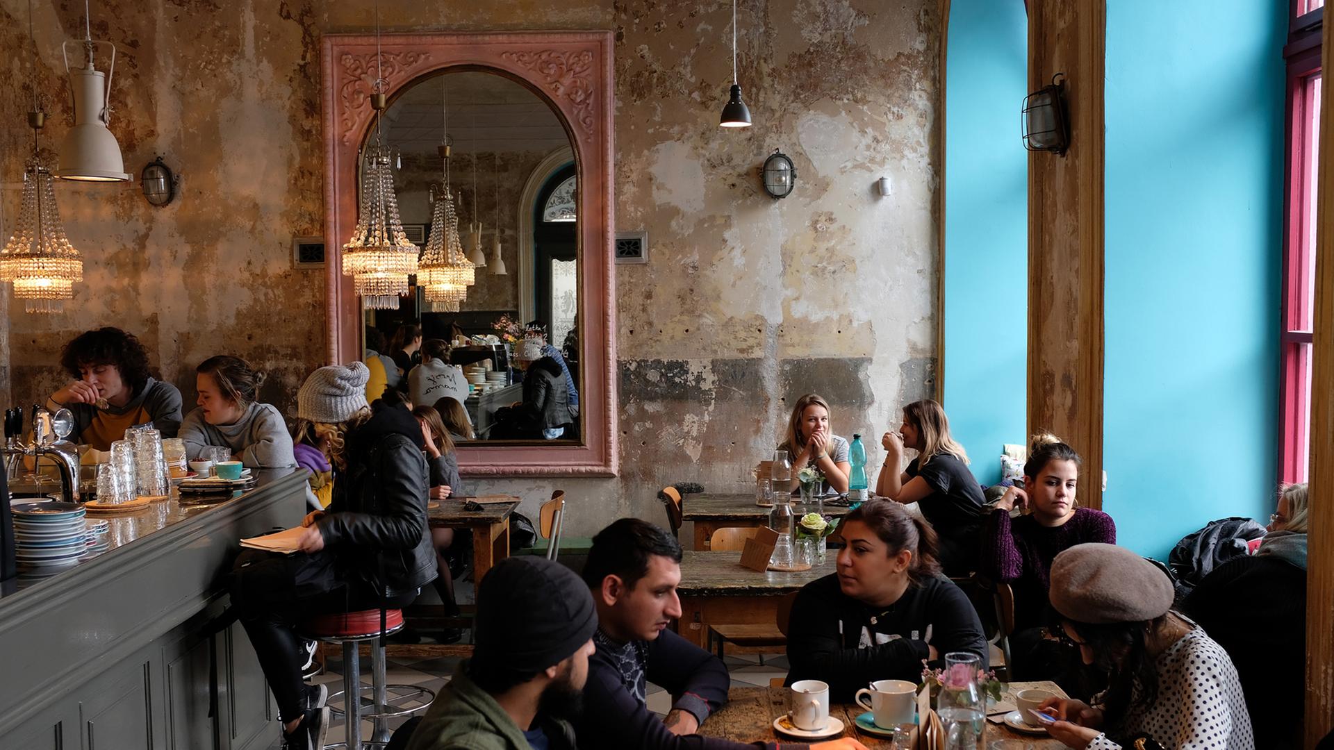 Menschen sitzen an Tischen vor den rustikalen Wänden eines Cafés Menschen sitzen an Tischen vor den rustikalen Wänden eines Cafés