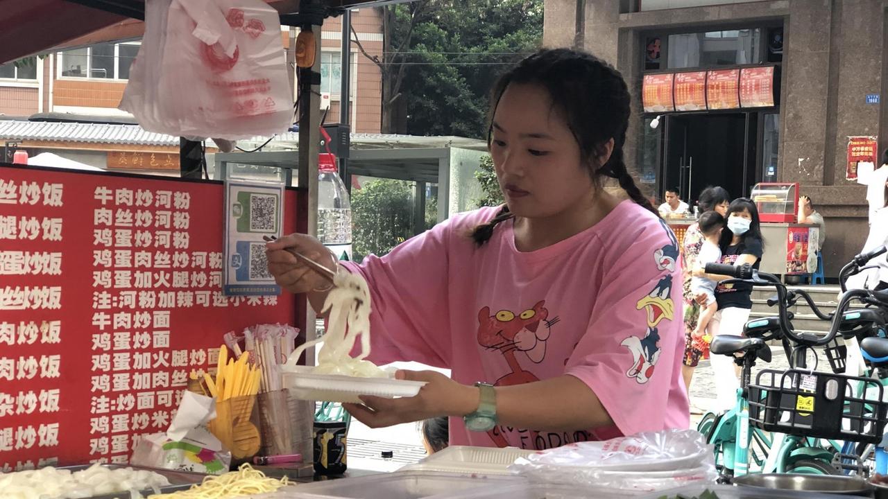 Eine junge Frau mit rosa T-Shirt bereitet auf einem Pappteller Essen zu. Eine junge Frau mit rosa T-Shirt bereitet auf einem Pappteller Essen zu.