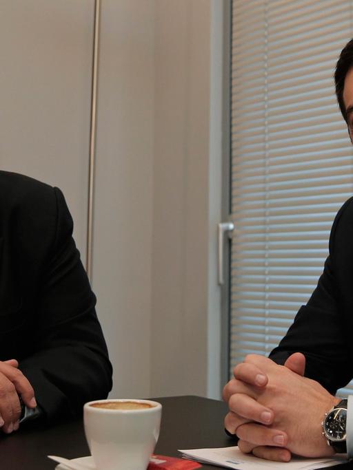 Panos Kammenos und Alexis Tsipras sitzen an einem Tisch und lächeln in die Kameras.