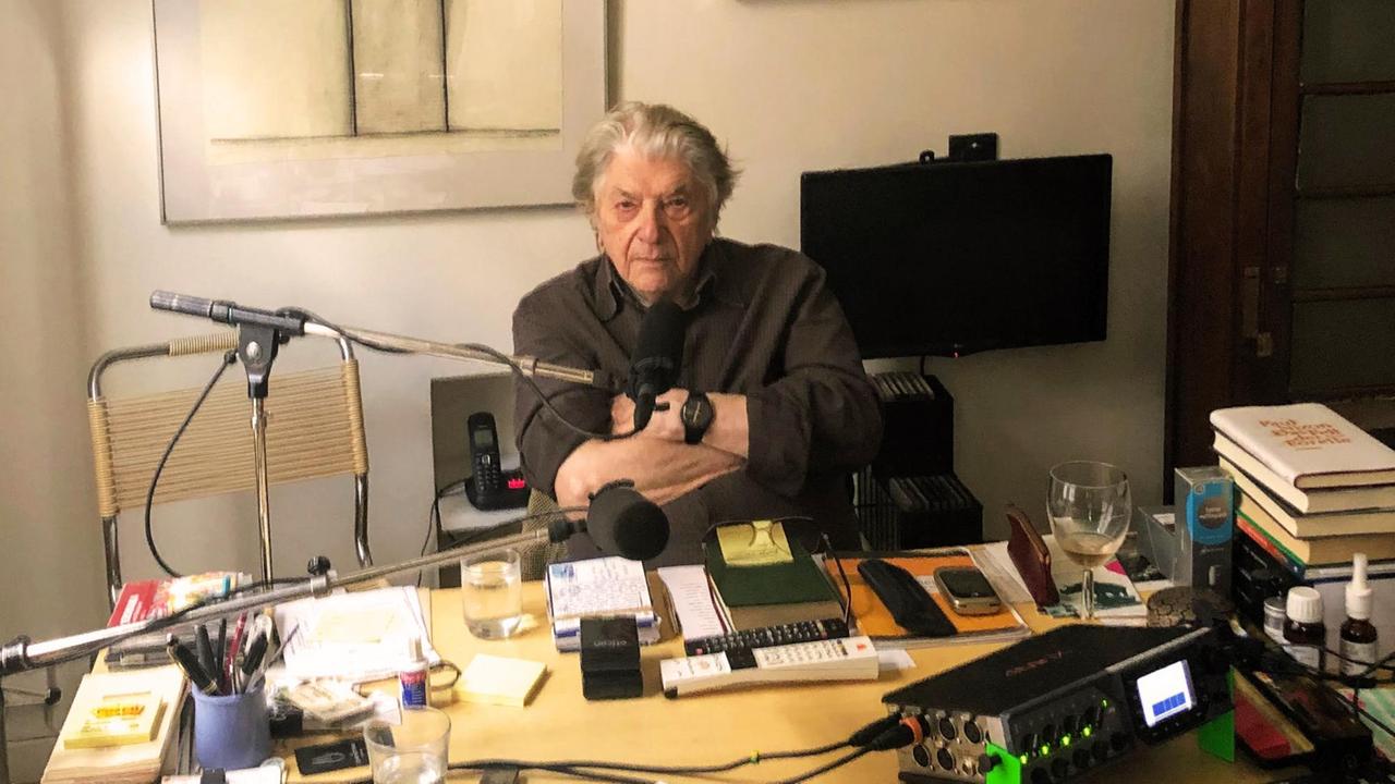 Paul Nizon sitzt an seinem Schreibtisch in seiner pariser Wohnung. Zahlreiche Gegenstände bevölkern die Schreibtischplatte.