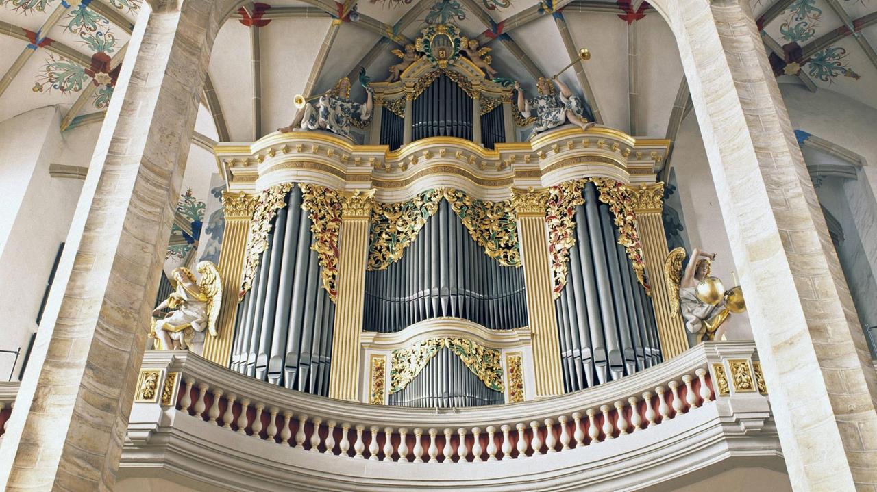 Blick von unten auf eine Orgelempore mit barock verziertem Instrument.