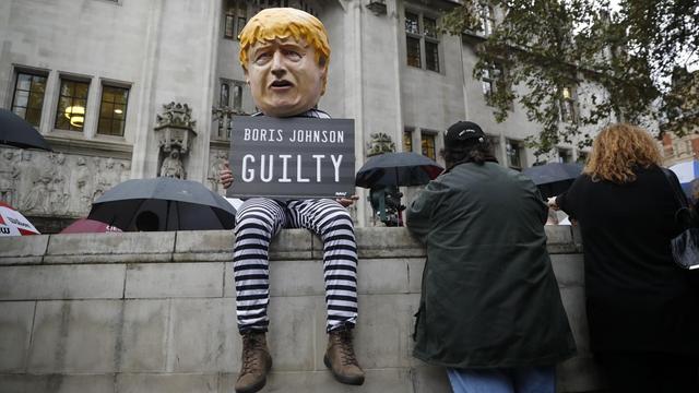 Ein Demonstrant im Sträflingsanzug und mit Boris-Johnson-Maske sitzt vor dem Supreme Court in London und hält ein Schild mit der Aufschrift "Boris Johnson: Schuldig".