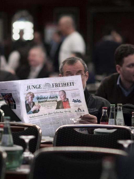 Ein Mann sitzt an einem Tisch und liest die Zeitung "Junge Freiheit".