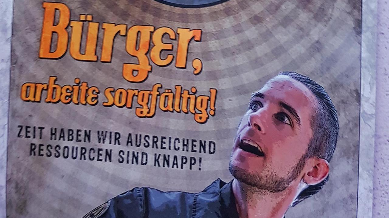 Ein Plakat zeiget einen Menschen in Uniform neben der Aufschrift: "Bürger, arbeitet sorgfältig! Zeit haben wir ausreichend. Ressourcen sind knapp!" Ein Plakat zeiget einen Menschen in Uniform neben der Aufschrift: "Bürger, arbeitet sorgfältig! Zeit haben wir ausreichend. Ressourcen sind knapp!"