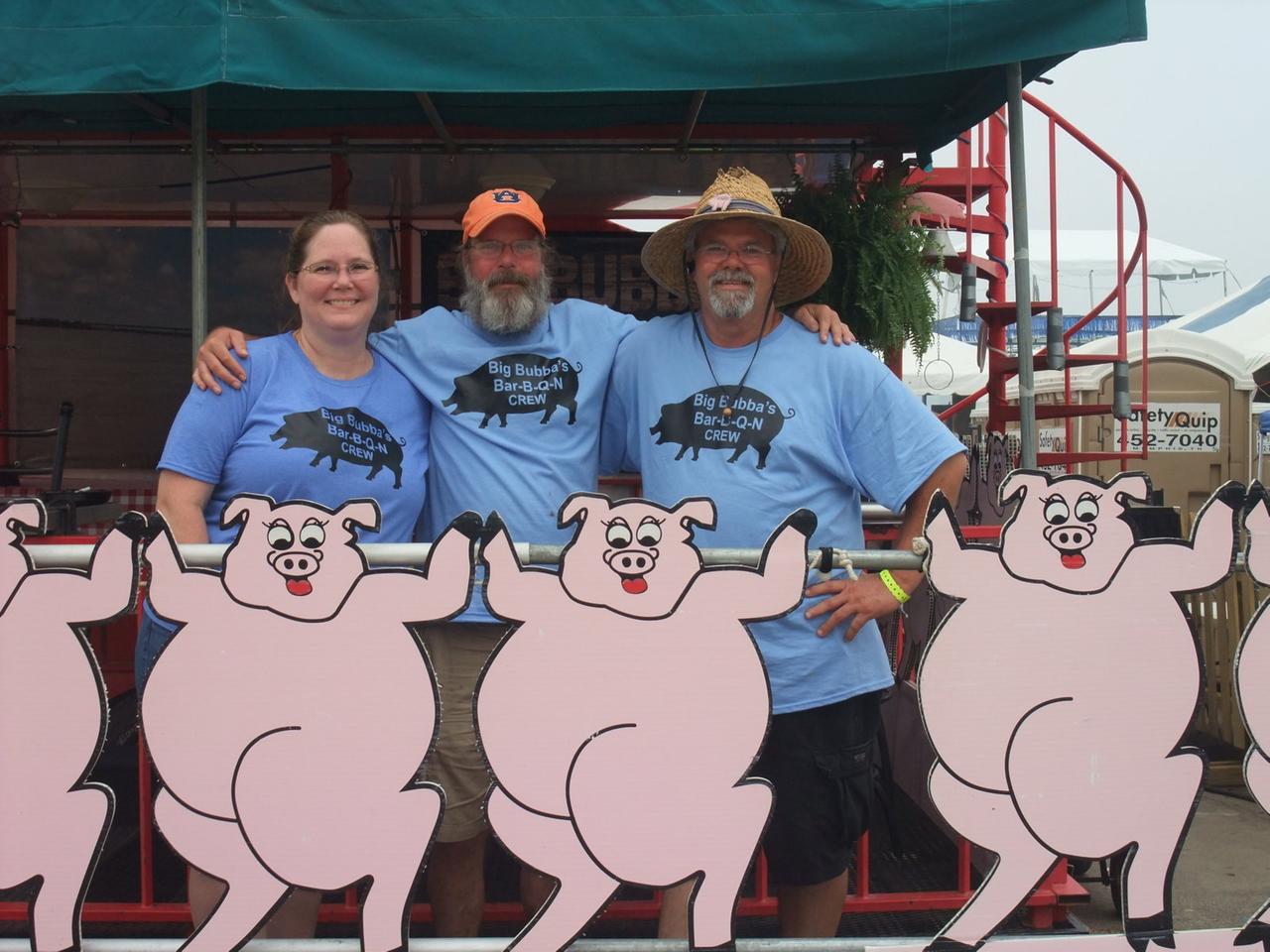 Zwei Männer und eine Frau stehen hinter einem Schild mit mehreren aufgereihten Schweinen.