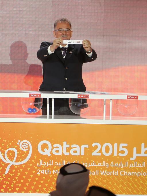 Leon Kalin, Mitorganisator der Handball-Weltmeisterschaft in Katar 2015 von der Internationalen Handball-Föderation (IHF), hält ein Los mit dem Namen von Katar bei der Ziehung der Spielpaarungen hoch.