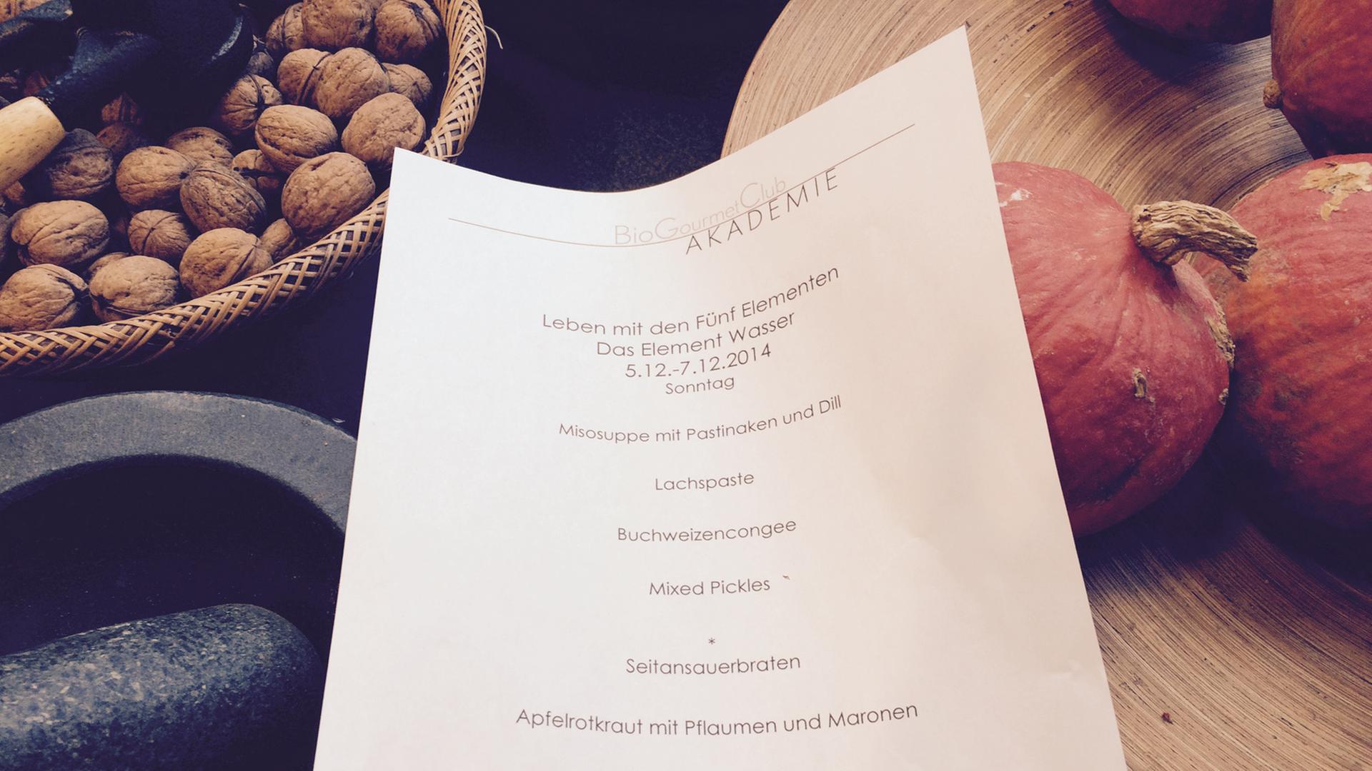 Ein Rezept liegt auf einem Tisch mit Kürbissen und Walnüssen.
