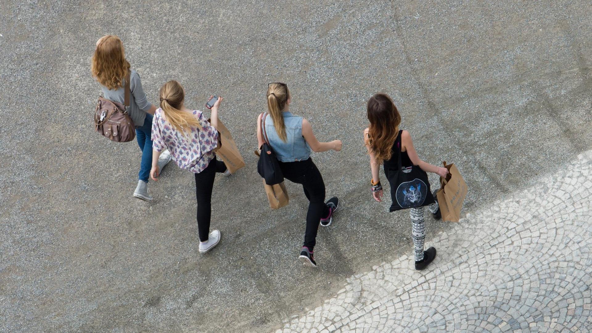 Vier Mädchen gehen mit Einkaufstaschen über einen Schotterweg. Vier Mädchen gehen mit Einkaufstaschen über einen Schotterweg.