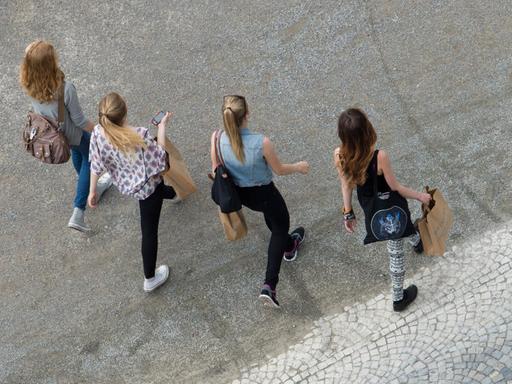 Vier Mädchen gehen mit Einkaufstaschen über einen Schotterweg.