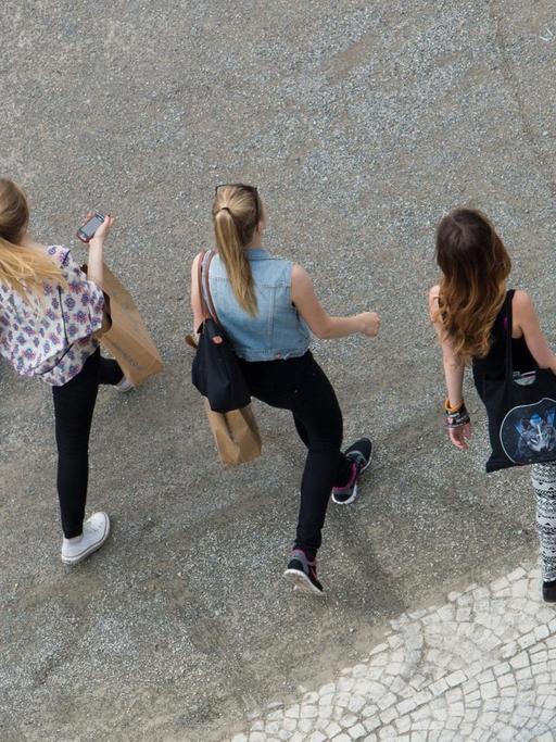Vier Mädchen gehen mit Einkaufstaschen über einen Schotterweg.