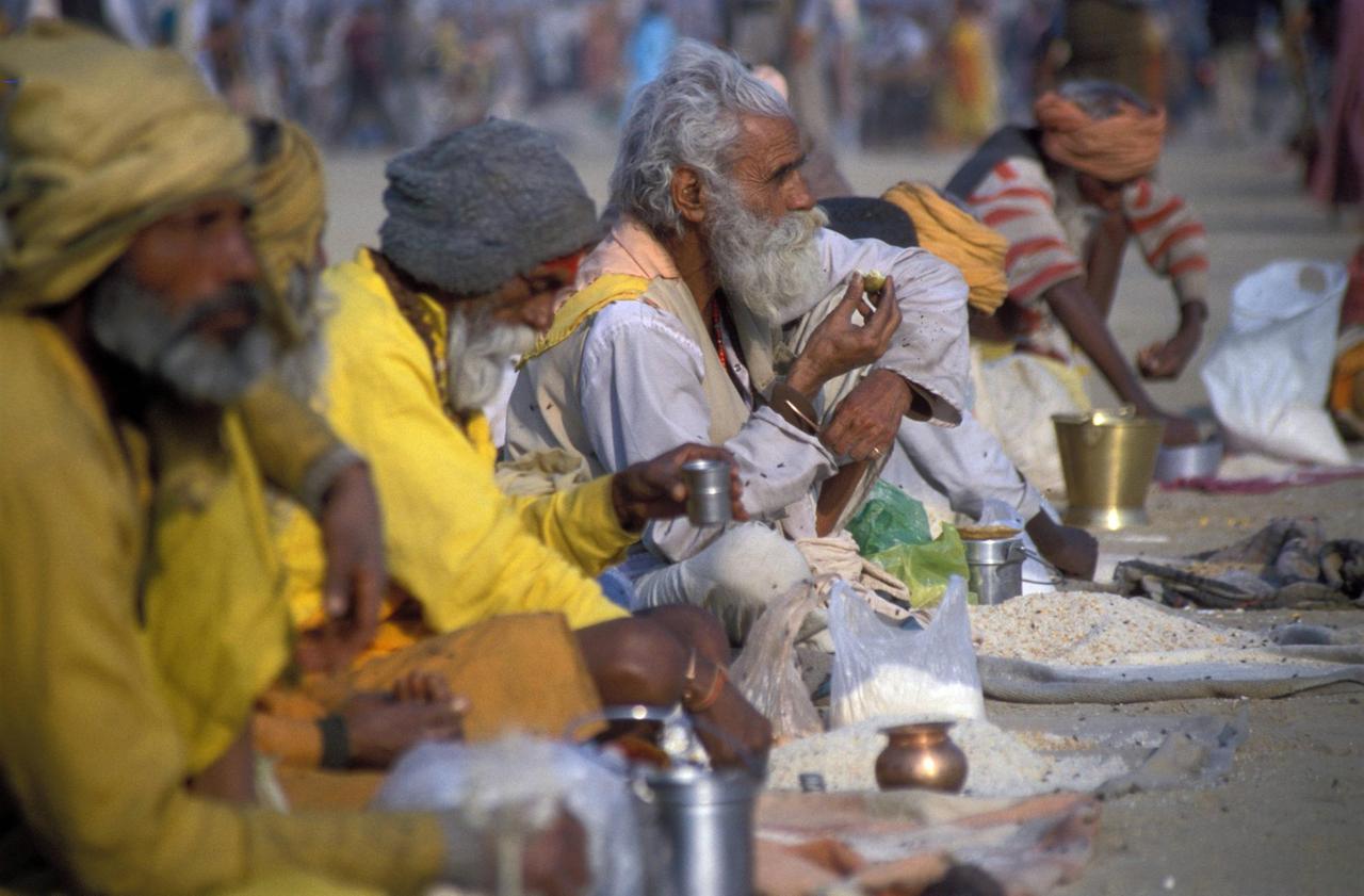 Hinduistische Bettelmönche in langen Gewändern sitzen auf dem Boden. Vor ihnen liegen ausgebreitete Tücher mit essen. Hinduistische Bettelmönche in langen Gewändern sitzen auf dem Boden. Vor ihnen liegen ausgebreitete Tücher mit essen.