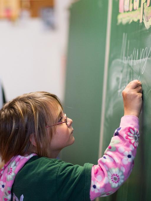 Die neunjährige Cora schreibt, beobachtet von Klassenlehrerin Anne John, in der Freien Schule in Bröbberow an die Schultafel.