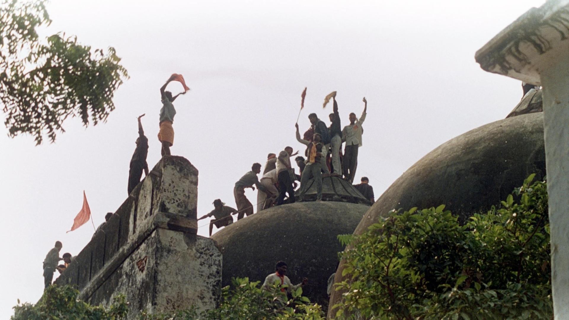 Jubelnde Hindus auf der Kuppel der eroberten Moschee. Radikale Hindus zerstörten am 6. Dezember 1992 die 1528 erbaute Babri-Moschee in Ayodhya im indischen Bundesstaat Uttar Pradesh, um an deren Stelle zu Ehren des Hindu-Gottes Rama einen Tempel zu errichten. Die dadurch entstandenen Unruhen forderten im ganzen Land rund 1200 Menschenleben. (Bild: picture-alliance / dpa) Jubelnde Hindus auf der Kuppel der eroberten Moschee. Radikale Hindus zerstörten am 6. Dezember 1992 die 1528 erbaute Babri-Moschee in Ayodhya im indischen Bundesstaat Uttar Pradesh, um an deren Stelle zu Ehren des Hindu-Gottes Rama einen Tempel zu errichten. Die dadurch entstandenen Unruhen forderten im ganzen Land rund 1200 Menschenleben. (Bild: picture-alliance / dpa)