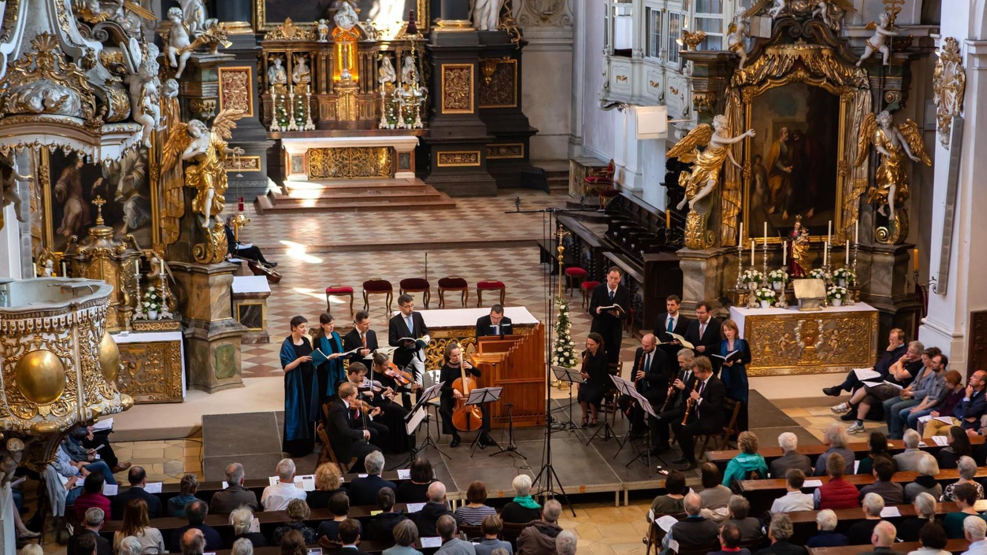 Das Ensemble Vox Luminis in der im Barock neu ausgestalteten Basilika St. Emmeram in Regensburg, die Sängerinnen und Sänger gruppieren sich um die Instrumente im Halbkreis.
