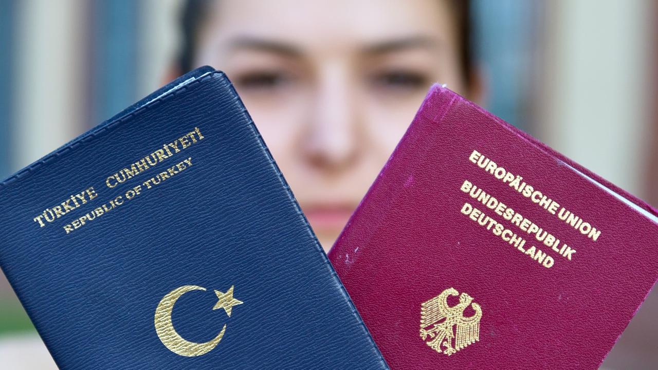 Eine junge Frau hält einen türkischen und einen deutschen Reisepass in den Händen. Eine junge Frau hält einen türkischen und einen deutschen Reisepass in den Händen.