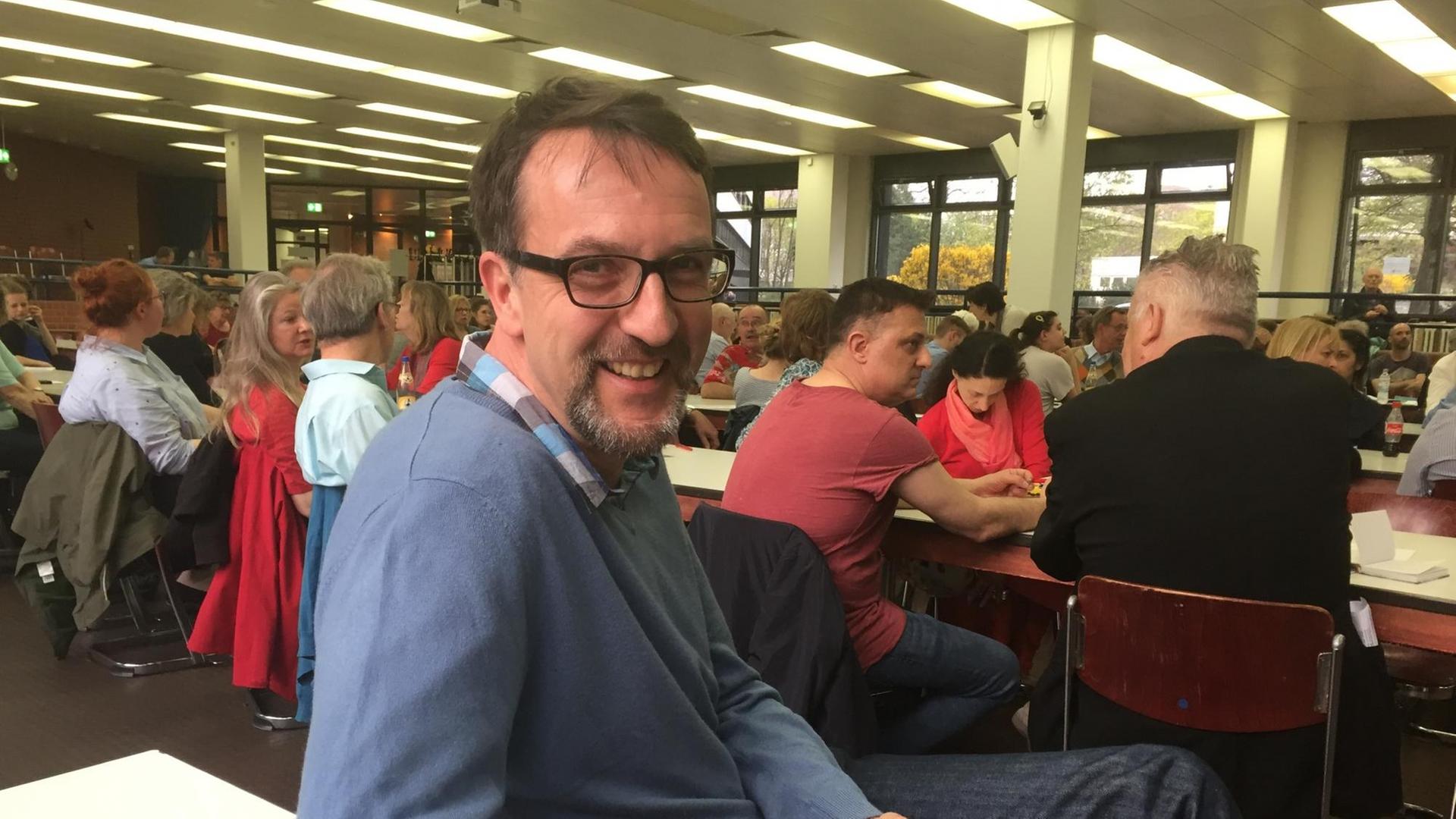 Ein Mann sitzt auf einem Stuhl vor einer Gruppe von Menschen und lächelt in die Kamera Ein Mann sitzt auf einem Stuhl vor einer Gruppe von Menschen und lächelt in die Kamera