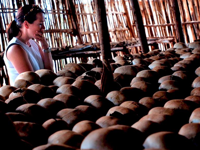 Eine Frau steht vor einer Schädelreihe: Gedenkstätte für den Völkermord in Ruanda