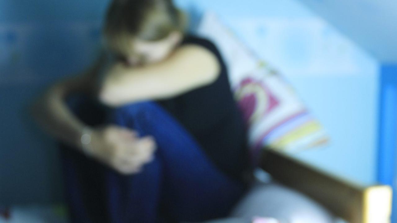 Eine verzweifelte junge Frau hockt auf einem Bett. Im Vordergrund: Tabletten. Eine verzweifelte junge Frau hockt auf einem Bett. Im Vordergrund: Tabletten.