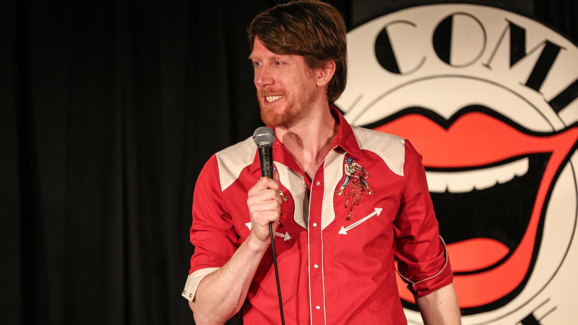 Der Komiker Christian Schulte Loh auf einer Bühne vor dem Logo des renommierten Londoner "Comedy Store"