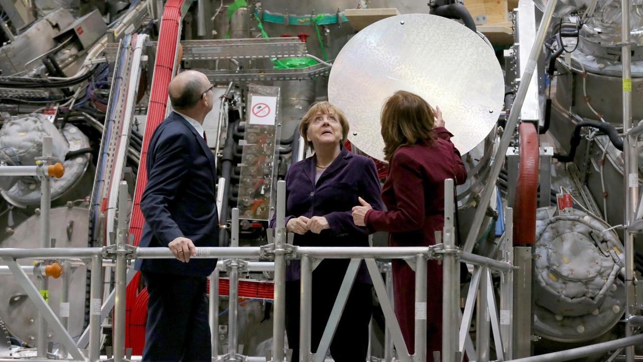 Bundeskanzlerin Angela Merkel (CDU) lässt sich am 03.02.2016 in der Kernfusions-Forschungsanlage "Wendelstein 7-x" in Greifswald (Mecklenburg-Vorpommern) nach der der erstmaligen Erzeugung von Wasserstoff-Plasma die Anlage von der wissenschaftlichen Direktorin des Max-Planck-Instituts für Plasmaphysik, Sibylle Günter, erklären Foto: Bernd Wüstneck/dpa ++ Bundeskanzlerin Angela Merkel (CDU) lässt sich am 03.02.2016 in der Kernfusions-Forschungsanlage "Wendelstein 7-x" in Greifswald (Mecklenburg-Vorpommern) nach der der erstmaligen Erzeugung von Wasserstoff-Plasma die Anlage von der wissenschaftlichen Direktorin des Max-Planck-Instituts für Plasmaphysik, Sibylle Günter, erklären Foto: Bernd Wüstneck/dpa ++