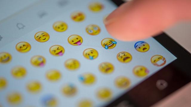Eine Frau tippt auf das Display eines Smartphones, auf dem zahlreiche Emojis zu sehen sind