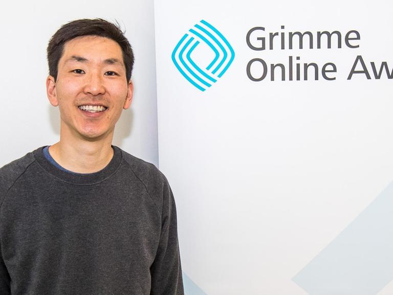 Frank Joung vor einem "Grimme Online Award"-Banner von der Bekanntgabe der Nominierungen zum Grimme Online Award 2018 am 26. April im "Startplatz" in Köln.