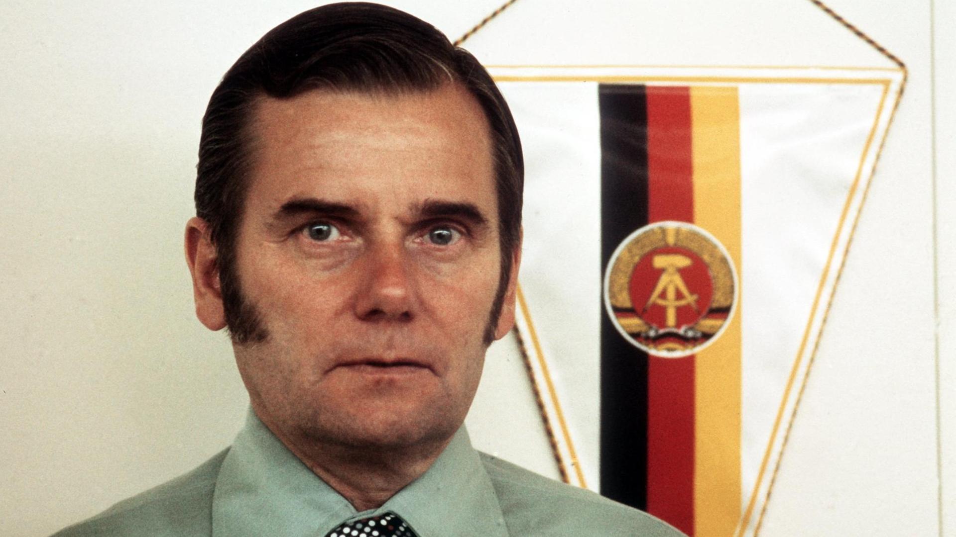 Porträt von Manfred Ewald, dem mächtigsten Mann im DDR-Sport. Im Hintergrund ist die Flagge der DDR zu sehen.