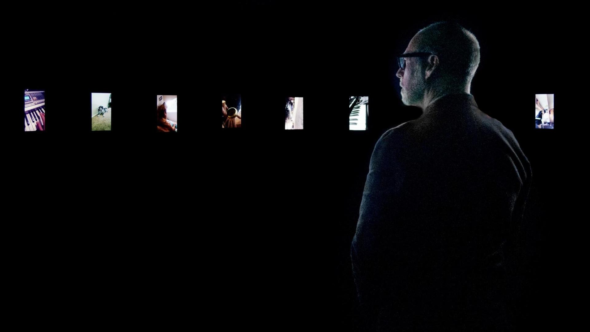Blick in die Ausstellung "Sound Stories" von Christian Marclay im Los Angeles County Museum of Art: Ein Mann betrachtet in einem dunklen Raum vor ihm leuchtene Handybildschirme