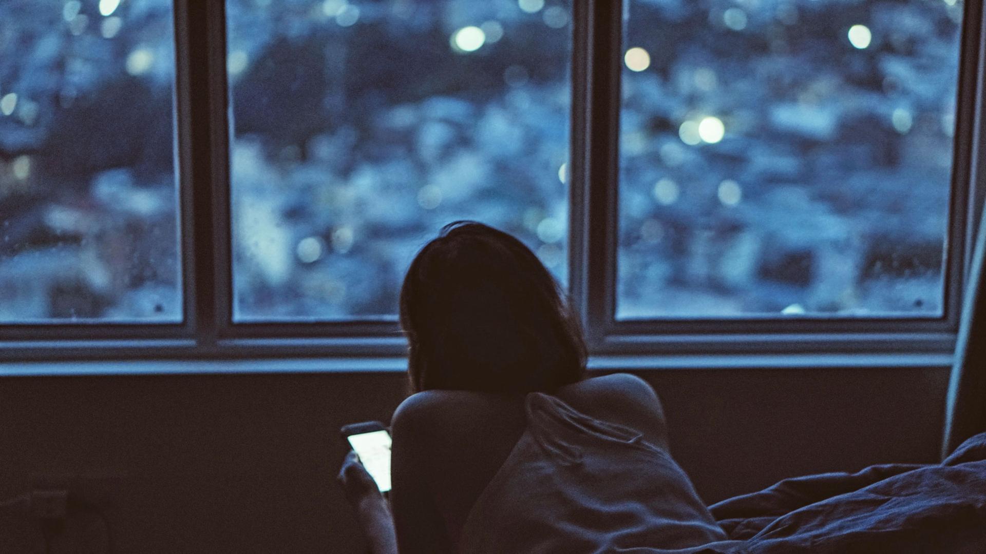 Eine junge Frau liegt bäuchlings im Bett und schaut auf ihr Smartphone. Eine junge Frau liegt bäuchlings im Bett und schaut auf ihr Smartphone.