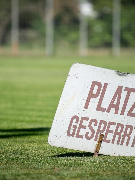 Ein Schild mit der Aufschrift "Platz gespresst" steckt im Rasen eines Vereinsspielfeldes