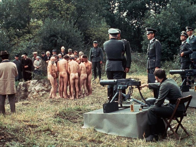 Filmszene: Nackte Männer, davor Wehrmachtssoldaten an Maschinengewehren