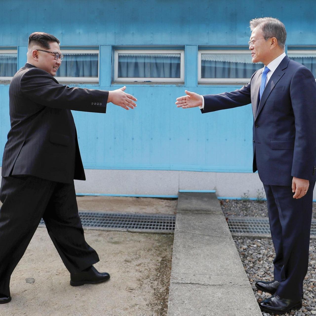 Die beiden schreiten vor einer blauen Hauswand lächelnd und mit vorgestreckten Händen aufeinander zu. Die beiden schreiten vor einer blauen Hauswand lächelnd und mit vorgestreckten Händen aufeinander zu.