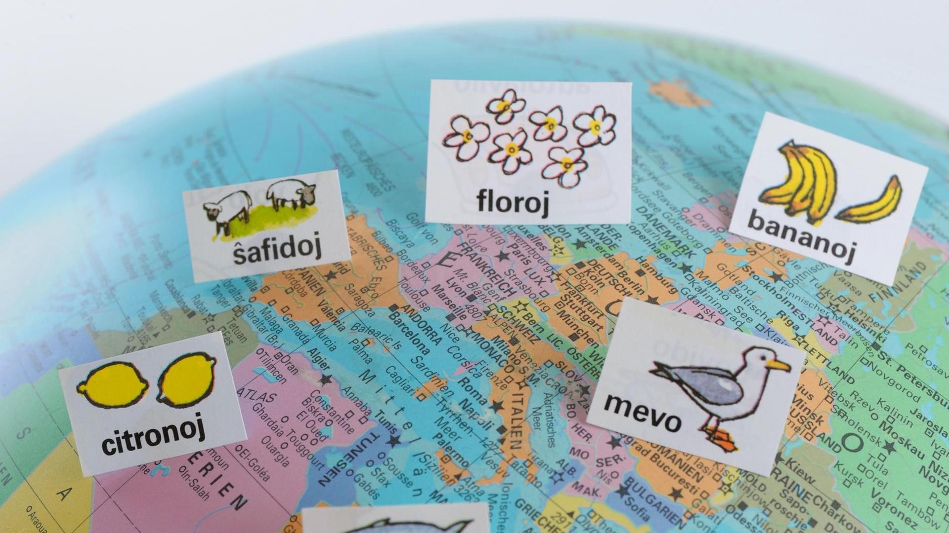 Auf einem Atlas, der Europa und einen Teil Afrikas zeigt, sind mehrere Zettel mit Esperanto-Wörtern verteilt Auf einem Atlas, der Europa und einen Teil Afrikas zeigt, sind mehrere Zettel mit Esperanto-Wörtern verteilt