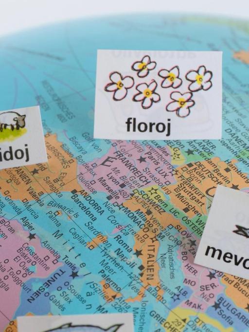 Auf einem Atlas, der Europa und einen Teil Afrikas zeigt, sind mehrere Zettel mit Esperanto-Wörtern verteilt