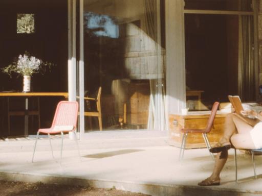 Eine Frau sitzt auf einem Stuhl und liest ein Buch. Das Bild ist vermutlich aus den 70er Jahren und der Zeit entsprechend atmosphärisch.
