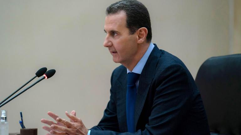 Der syrische Machthaber al-Assad sitzt vor einem Mikrofon.
