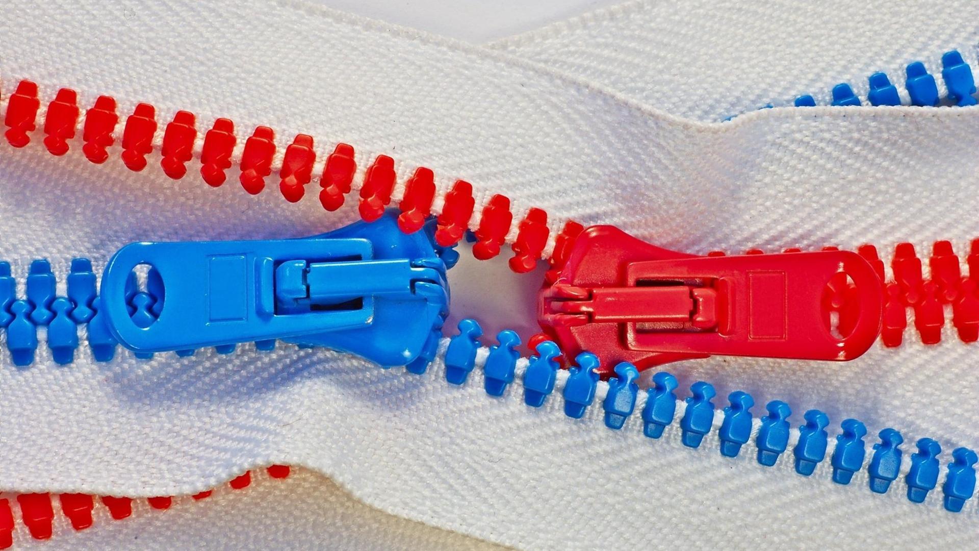Ein roter und ein blauer Reißverschluss greifen ineinander.