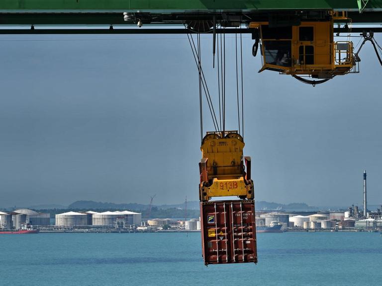 Ein Container schwebt am Verladekran über dasa türkisblaue Meer vor Singapur.