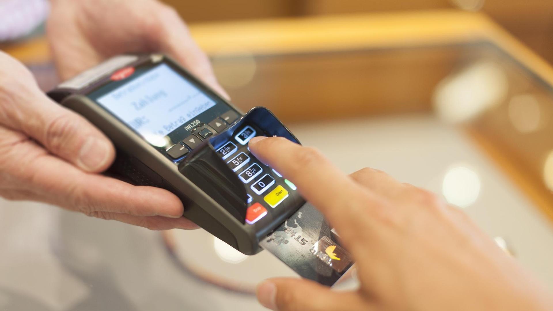 Eine Person bedient ein Lesegerät zur elektronischen Zahlung mit EC- oder Kreditkarte. Eine Person bedient ein Lesegerät zur elektronischen Zahlung mit EC- oder Kreditkarte.