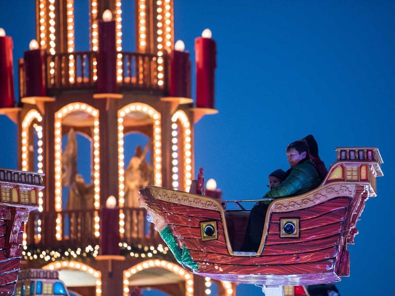 Besucher sitzen am 01.12.2017 auf dem eröffneten Weihnachtsmarkt an der Landsberger Allee in Berlin in einem Kinder-Karussell. Nach Veranstalterangaben steht auf dem Rummelplatz in Berlin-Lichtenberg neben zahlreichen Fahrgeschäften die mit 26,5 Meter Höhe größte Weihnachtspyramide der Welt.