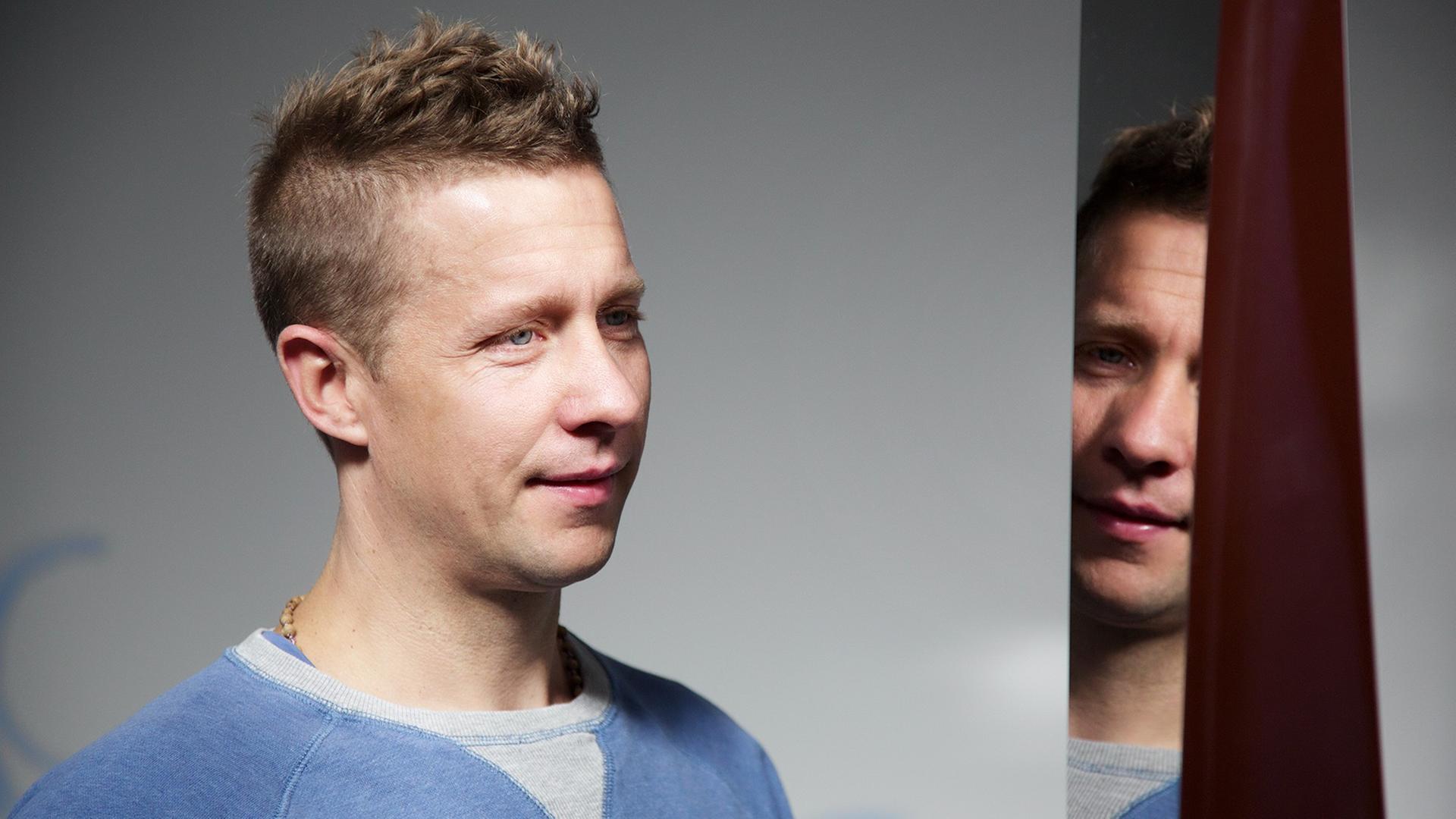 Portrait von Jeppe Hein, der vor einem Spiegel steht und sich teilweise darin spiegelt. Portrait von Jeppe Hein, der vor einem Spiegel steht und sich teilweise darin spiegelt.