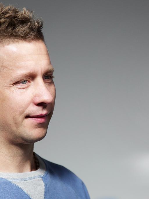 Portrait von Jeppe Hein, der vor einem Spiegel steht und sich teilweise darin spiegelt.