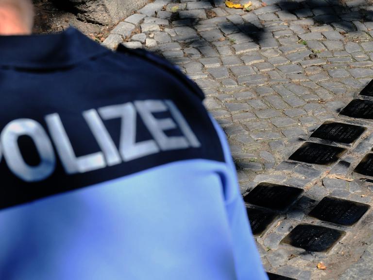 Eine Polizistin betrachtet die von Unbekannten mit schwarzer Farbe beschmierten "Stolpersteine" in Berlin-Friedenau.