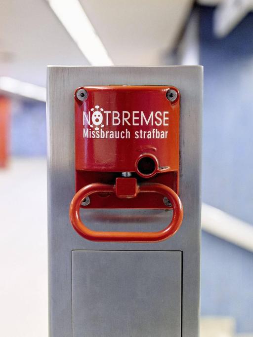 Eine Notbremse auf einem Bahnsteig mit einem Coronavirus an Stelle des "O".