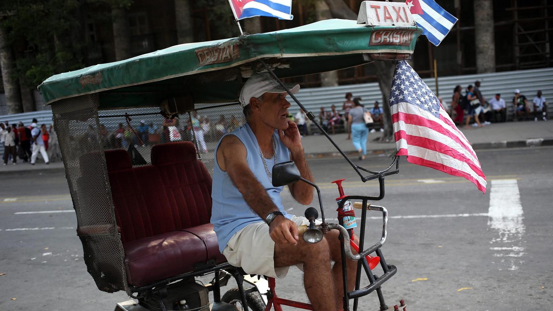 Auf dem Bild ist ein Radfahrer in Havanna zu sehen, der die kubanische und die US-Flagge an seinem Rad befestigt hat. Auf dem Bild ist ein Radfahrer in Havanna zu sehen, der die kubanische und die US-Flagge an seinem Rad befestigt hat.