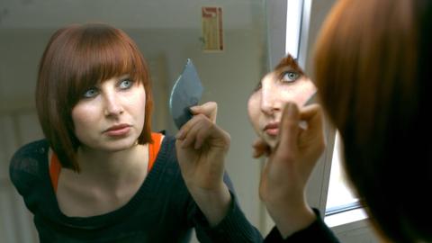 Eine Frau blickt in einen Spiegel.